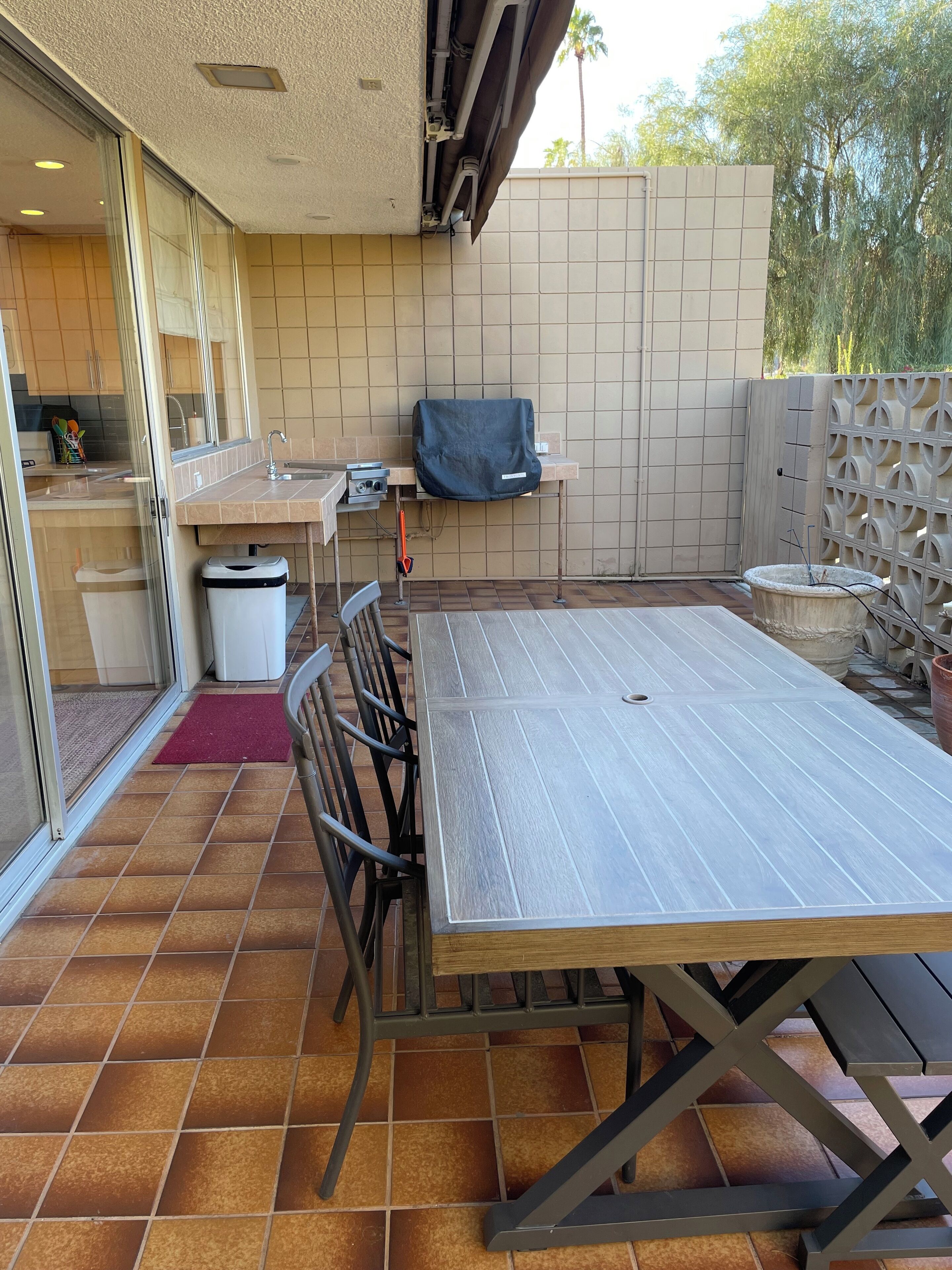 Een terras met een tafel, stoelen, een barbecue en een buitenkeuken met een spoelbak en kastjes.