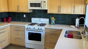 A modern kitchen with wooden cabinets, a stainless steel stove, a microwave, and a sink.