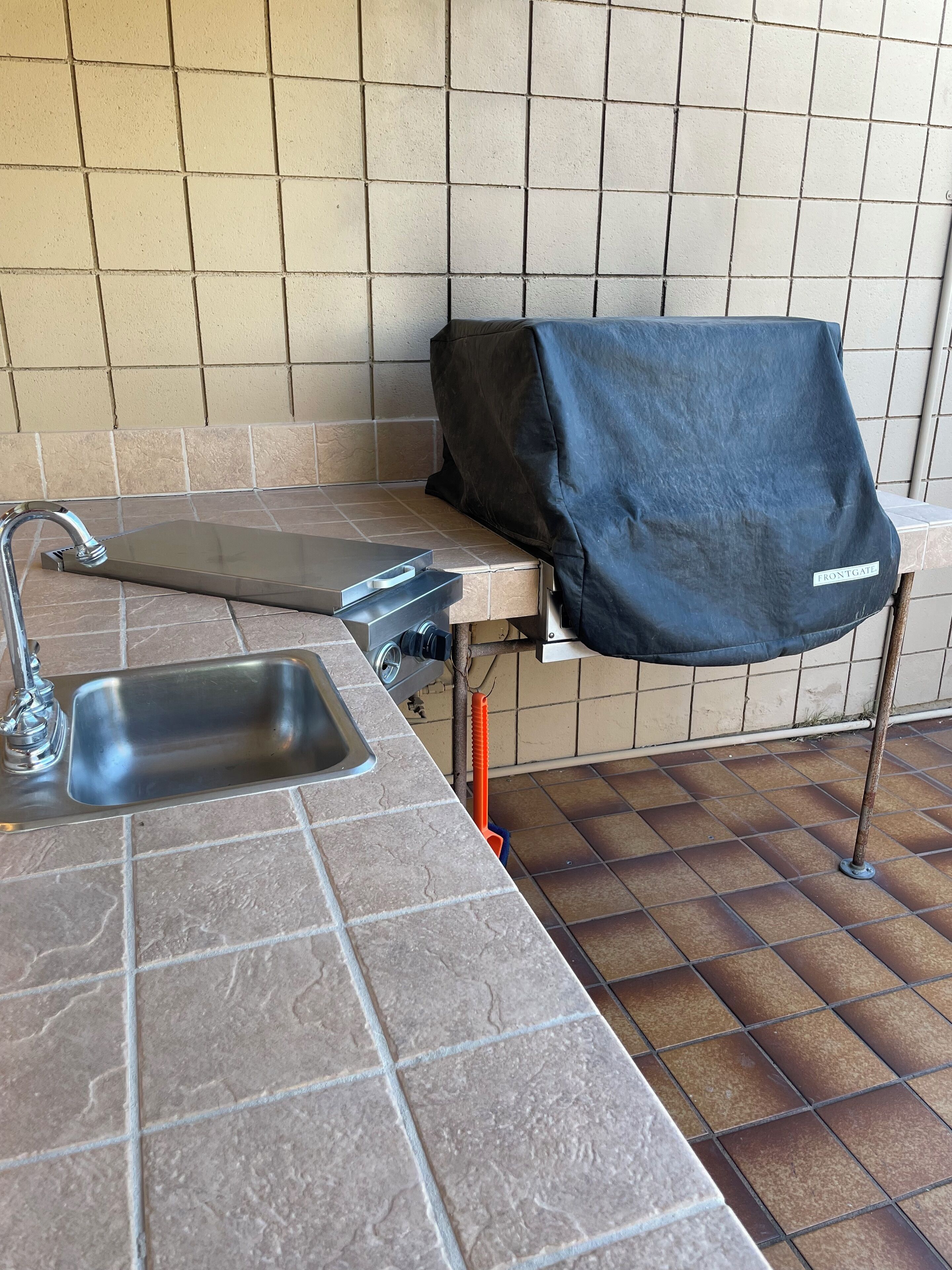 A kitchen area with a sink, a countertop, and a grill cover labeled "FRONTGATE."