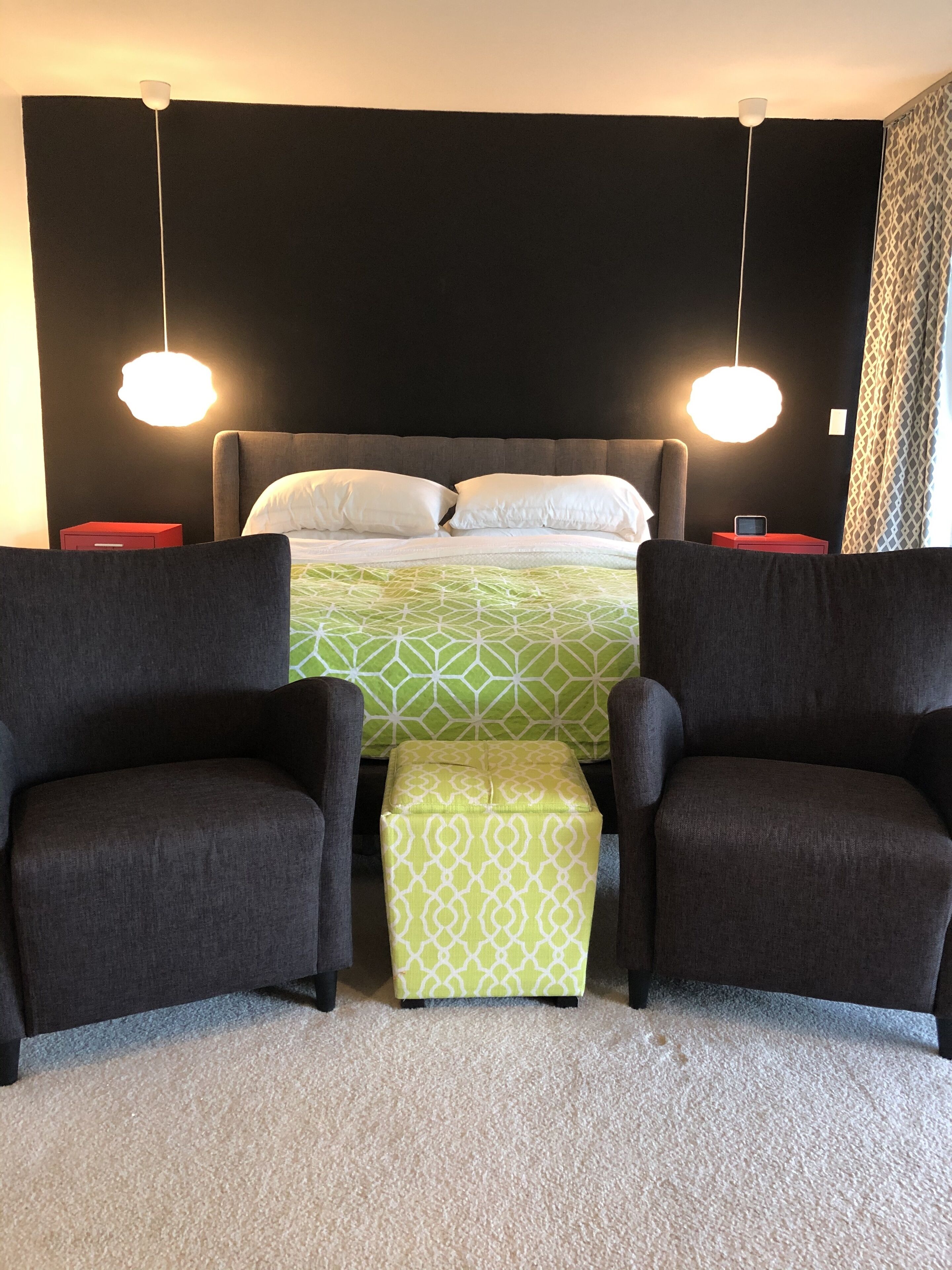 Une chambre à coucher comprenant un lit, deux tables de chevet, deux fauteuils, un banc et une tête de lit.