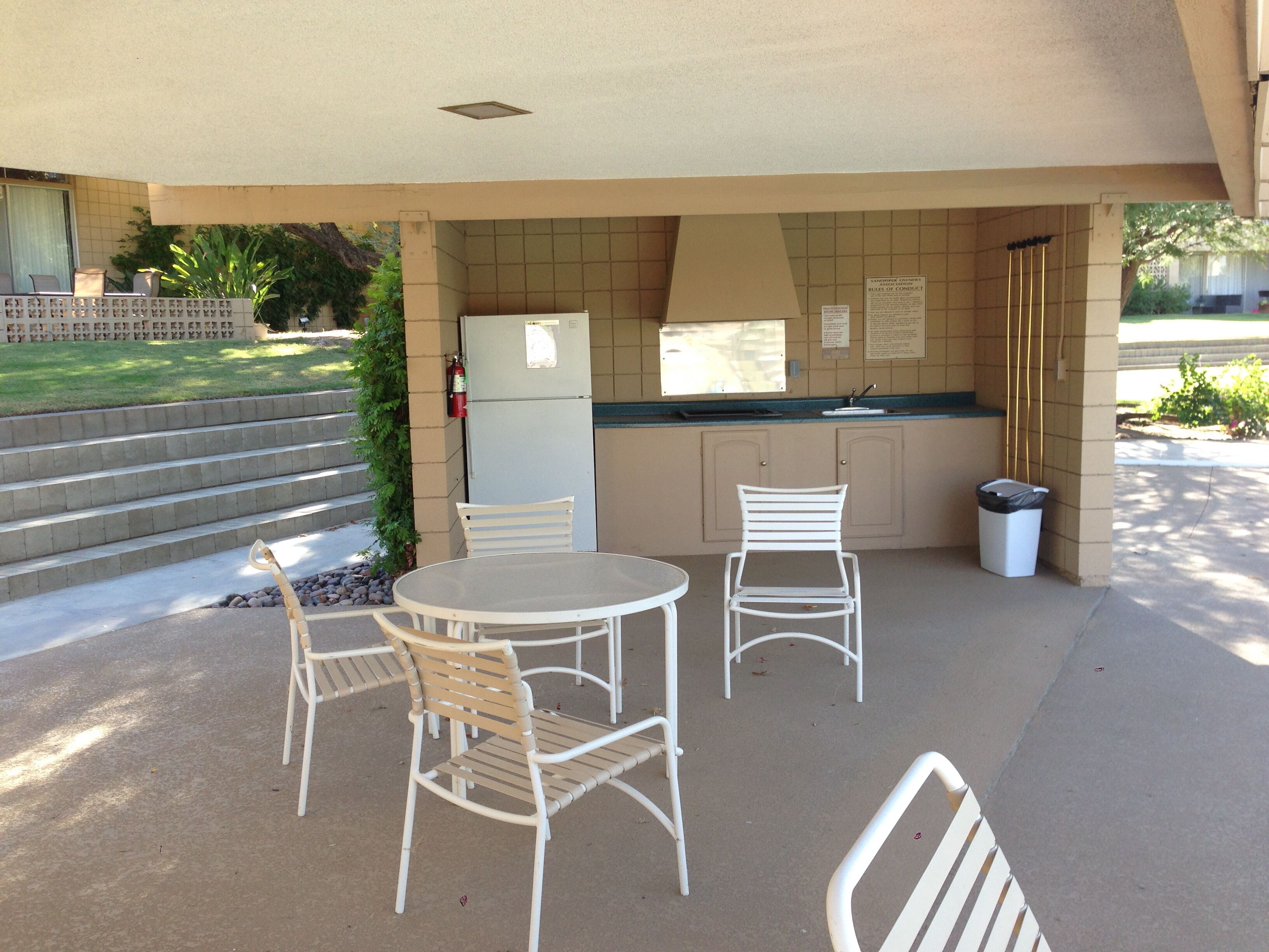 Patio esterno con tavolo, sedie, frigorifero e cestino.