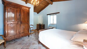 A bedroom with a large wooden wardrobe, a bed with white linens, a wooden chair, and a chandelier.