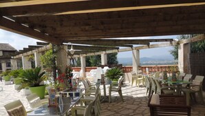 Une terrasse extérieure avec des tables et des chaises, entourée de plantes en pot et dotée d’un sol en pierre.
