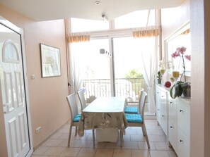 Uma sala de jantar com mesa e cadeiras, uma janela com cortinas e vista para o exterior.