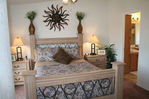 Un dormitorio con cama, mesitas de noche, lámparas, un adorno de sol y un espejo.