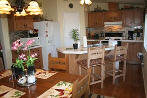 Una cocina con armarios de madera, un refrigerador blanco, un fregadero y un comedor con mesa y sillas.