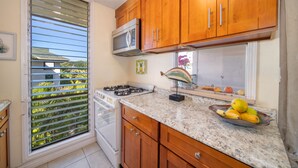 A kitchen with wooden cabinets, a microwave, a gas stove, and a bowl of fruit on the counter.
