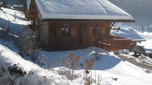 Een houten hut met een sneeuwbedekte dak, omringd door besneeuwde grond en bergen op de achtergrond.