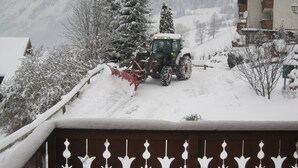 Een besneeuwd landschap, met een tractor die sneeuw van een oprit ruimt.