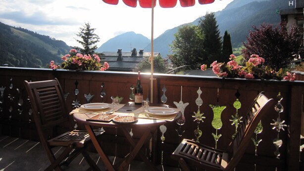 Een terras met een tafel voor twee personen, een houten stoel en een grote gestreepte parasol.
