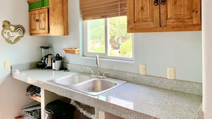 A kitchen with granite countertops, wooden cabinets, a double sink, a window with a view, and a hanging plant. - Villa Sunset, Ocean View rooftop, just 3 blocks from the beach (San Pancho)