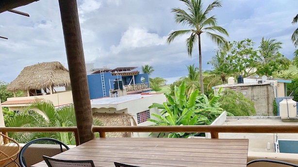A wooden table and chairs on a terrace with a view of a building and palm trees. - Villa Sunset, Ocean View rooftop, just 3 blocks from the beach (San Pancho)