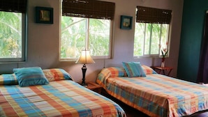 A room with two beds, each with a colorful checkered bedspread and matching pillows, a bedside table with a lamp, and windows with blinds. - Villa Sunset, Ocean View rooftop, just 3 blocks from the beach (San Pancho)