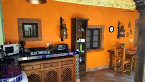 A kitchen with a tiled backsplash, wooden cabinets, a microwave, a stove, and a dining area with a wooden table and chairs. - Casa de Como Casita #2 - Ajijic Village (Ajijic)