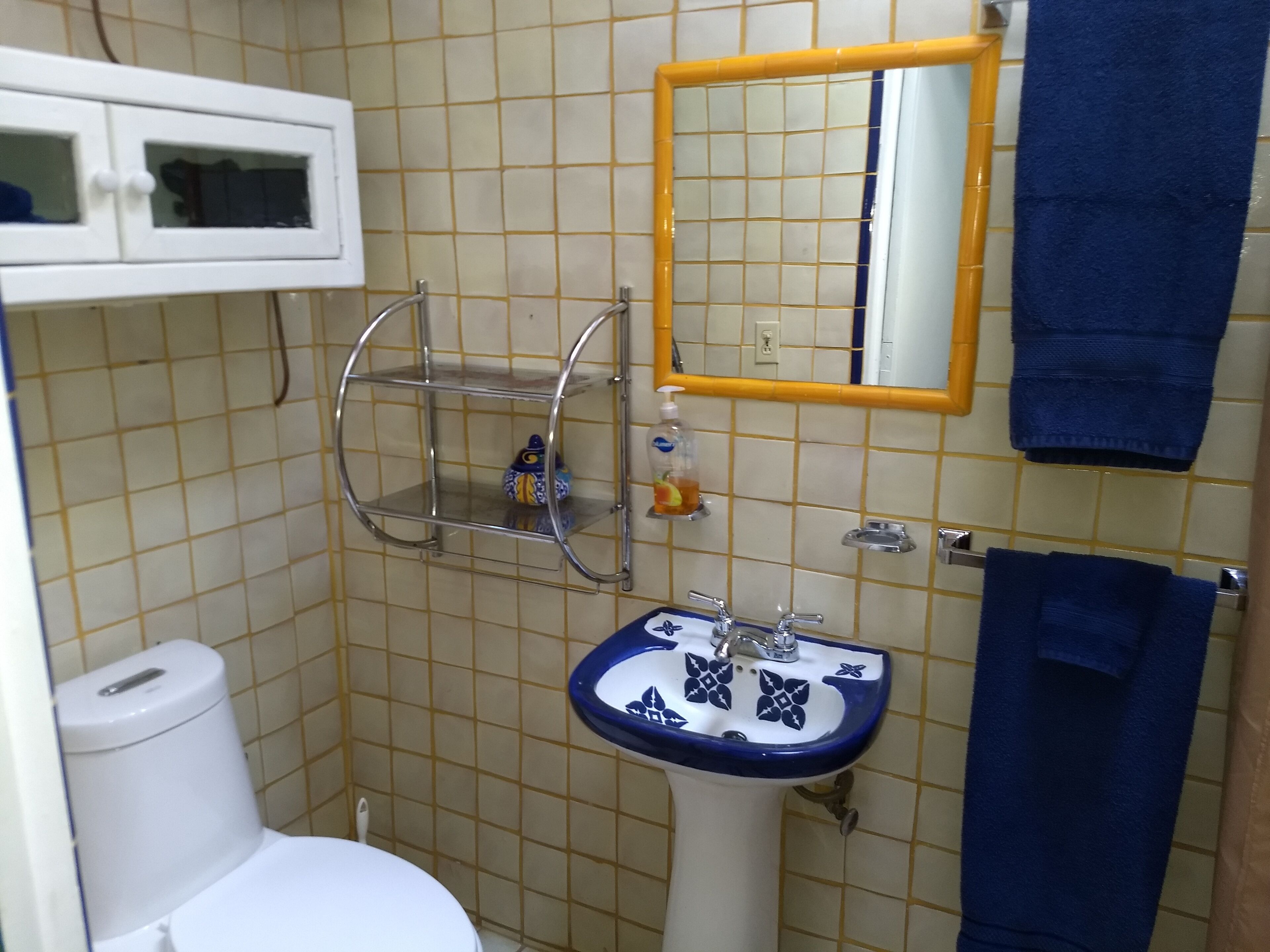 A bathroom with a white toilet, a blue and white sink, a mirror with a yellow frame, and a blue towel hanging on a rack.