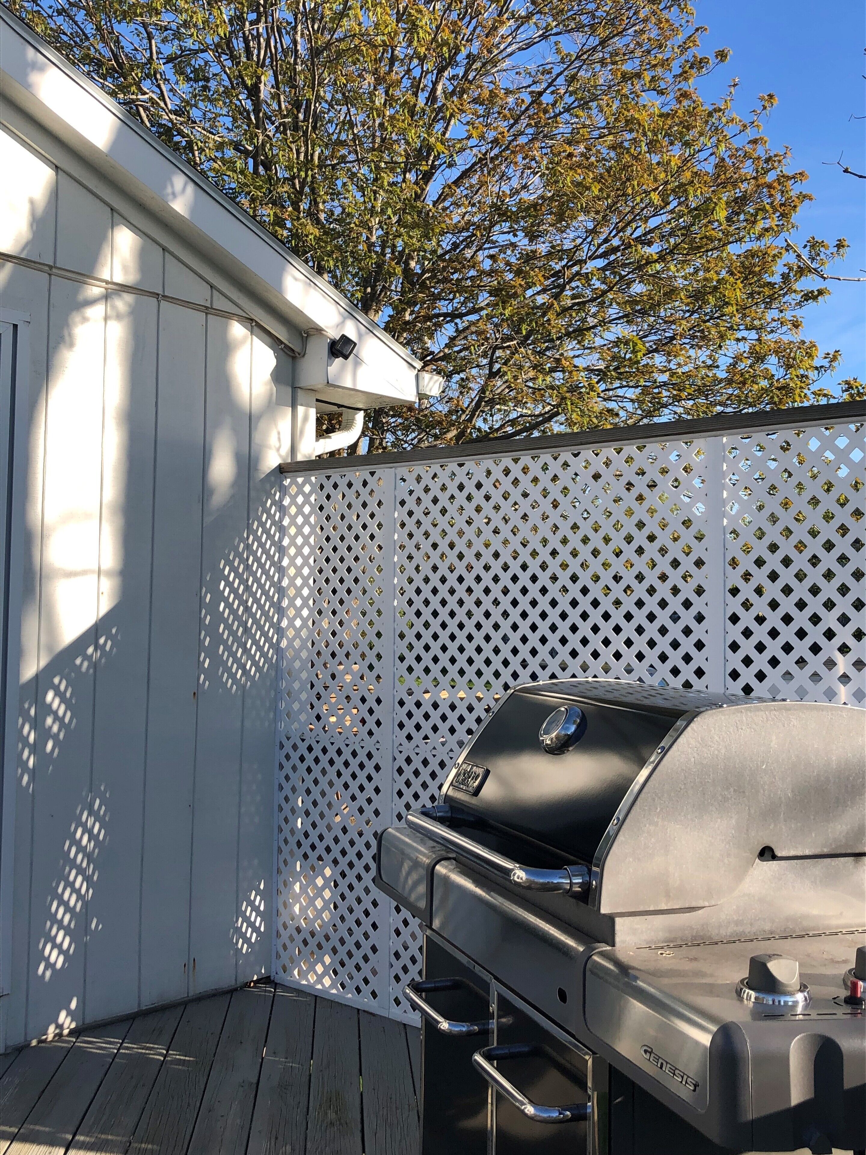 A patio area with a white fence, a wooden deck, and a black Genesis grill.