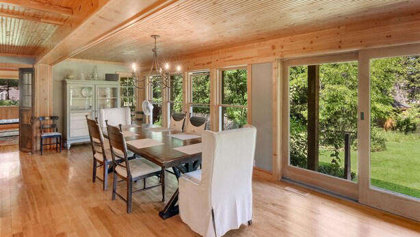 Uma sala de jantar espaçosa com mesa e cadeiras de madeira, amplas janelas com vista para o exterior e um lustre moderno.