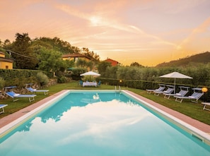 Ein rechteckiger Pool mit Liegestühlen und Sonnenschirmen, umgeben von Grünflächen und Hügeln.