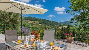 A breakfast setup on an outdoor table with a scenic view, including a table umbrella, chairs, and a variety of breakfast items. - Tenuta Bellosguardo on the hills with Swimming pool and Jacuzi! EXCLUSIVE ESTATE (Lucca)