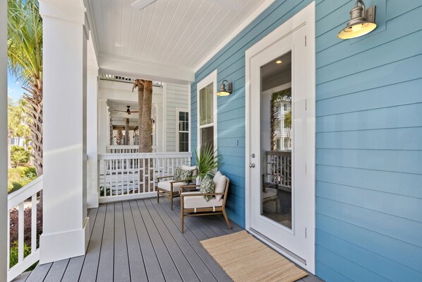 A covered porch with a white railing, a seating area with two chairs, and a door leading to a room with a glass door. - Marshall Cottage - Gulf Views from 3rd Floor Balcony! Free Bikes/Fitness/Tennis (Seacrest Beach)