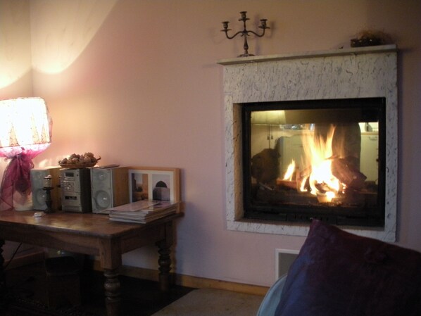 Una sala de estar acogedora con chimenea, una mesa con libros y una lámpara, y un candelabro en la pared.