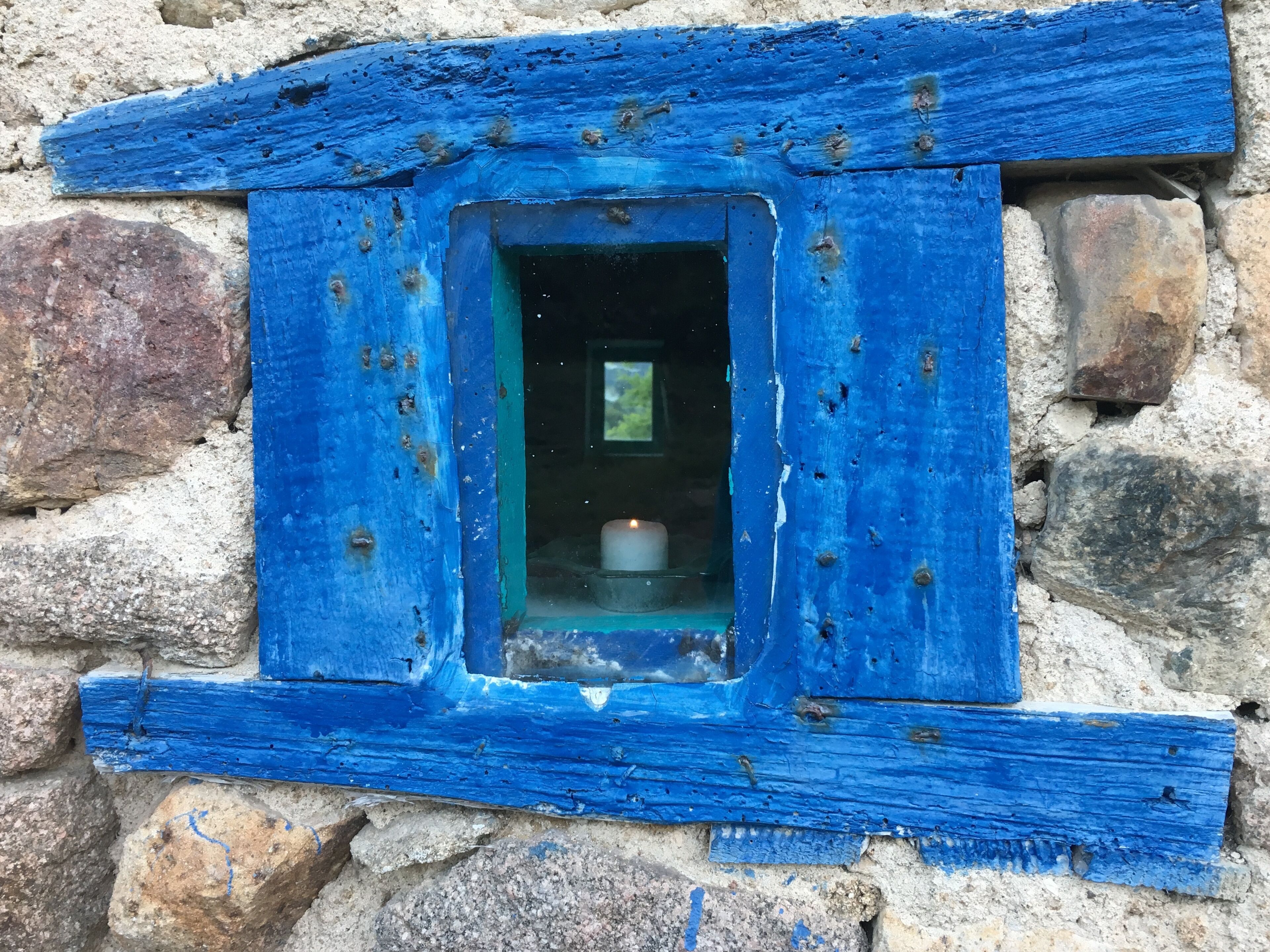 Eine rustikale Steinmauer mit einem kleinen, blau gestrichenen Fenster.