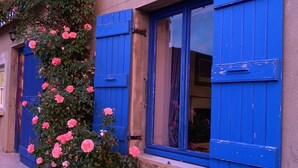 Un bâtiment avec des volets bleus et des rosiers roses.