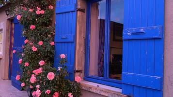 Un bâtiment avec des volets bleus et des rosiers roses.