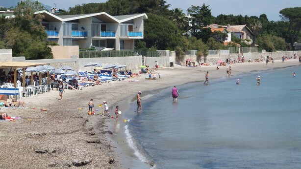 Een strand met parasols, ligbedden en mensen.