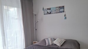 Een slaapkamer met een bed, gordijnen, een wandlamp en een klein nachtkastje.