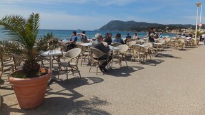Een terras met tafels en stoelen met uitzicht op een strand en zee.
