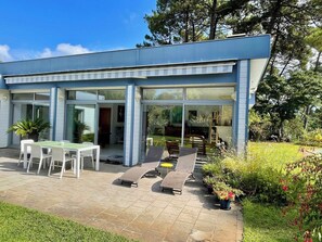 A modern house with a patio area featuring a table, chairs, and sun loungers. - Lovely house with pool & beautiful garden G0287 (Lacanau)