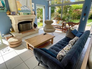 Ein Wohnzimmer mit Kamin, einer Couch, einem Couchtisch und Blick auf den Garten.