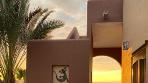 Een gebouw met een muurschildering van een hagedis, een betonnen pad en uitzicht op de oceaan bij zonsondergang.