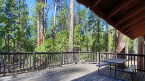 A wooden deck with picnic tables, surrounded by tall trees.