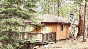 A cabin with a wooden deck and stone chimney, surrounded by trees.