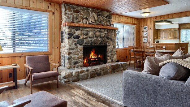A stone fireplace with a fire, wooden furniture, and a kitchen area.