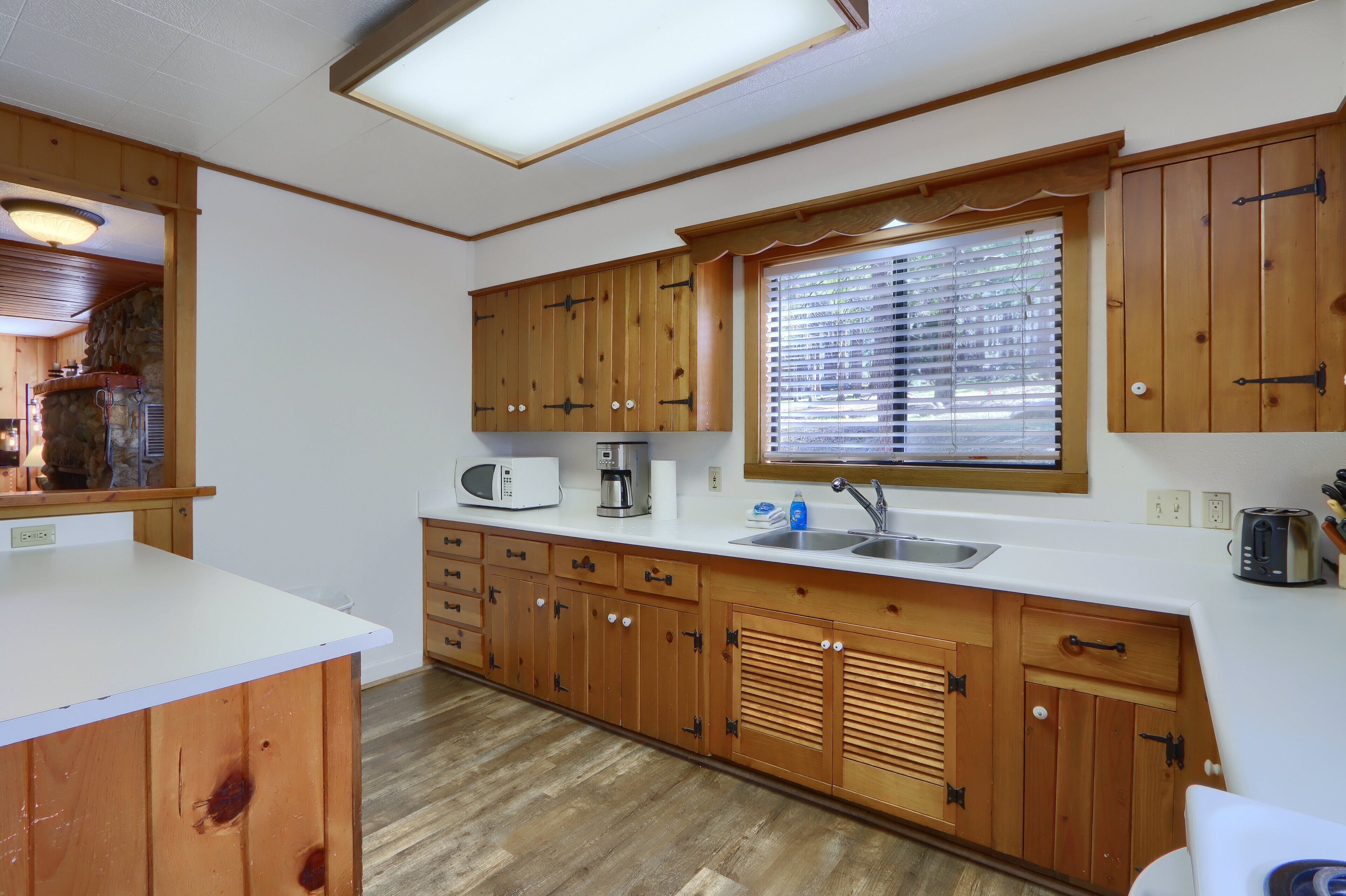A compact kitchen with wooden cabinets, a microwave, a coffee maker, and a window with blinds.