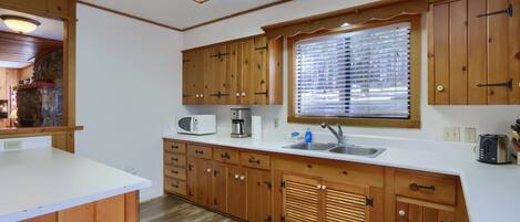 A compact kitchen with wooden cabinets, a microwave, a coffee maker, and a window with blinds.
