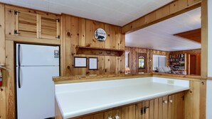A cabin interior with wooden walls, a white refrigerator, a wooden counter, and a bookshelf.