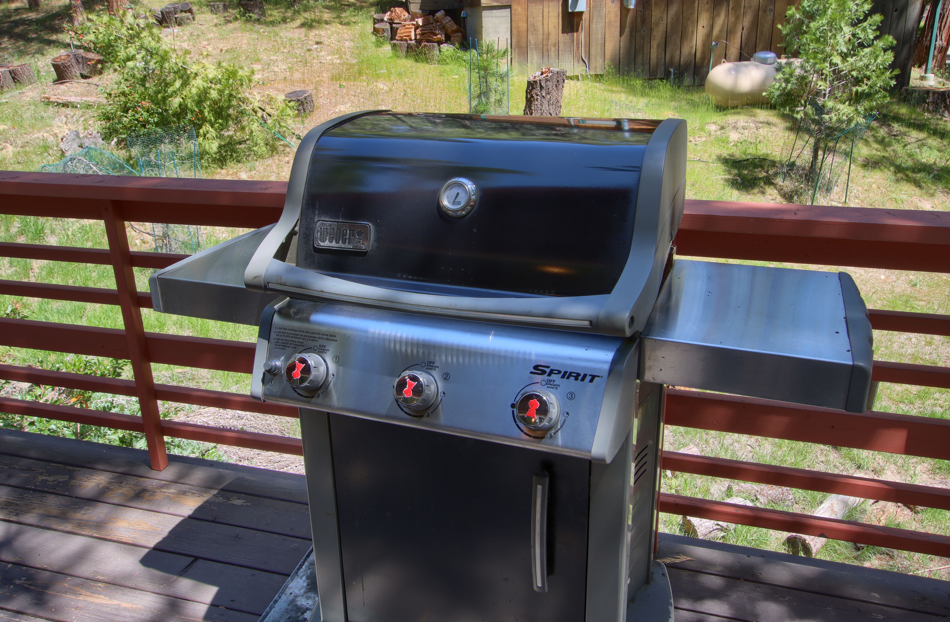 Una parrilla para barbacoa con dos perillas de control y el logotipo de Spirit, sobre una terraza de madera con barandilla roja.