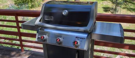 Una parrilla para barbacoa con dos perillas de control y el logotipo de Spirit, sobre una terraza de madera con barandilla roja.
