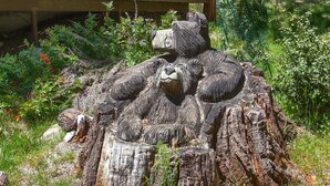 Una gran escultura de madera con osos sobre un tocón en un jardín.