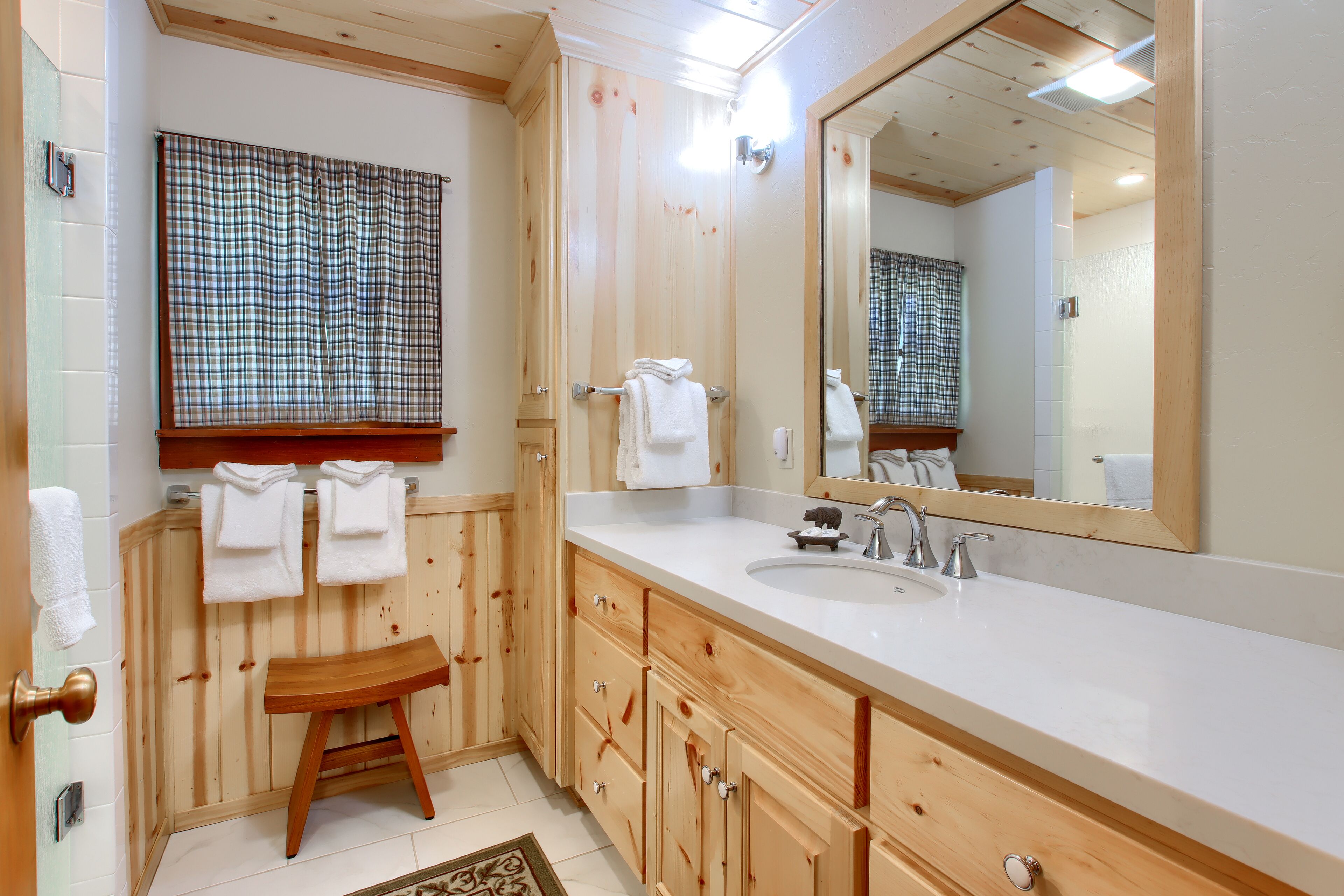 Une salle de bain avec des meubles en bois, un lavabo, un miroir et une fenêtre agrémentée de rideaux à carreaux.