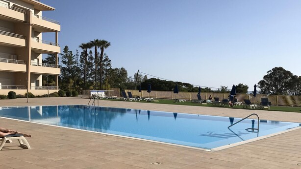 A swimming pool with lounge chairs and umbrellas, surrounded by a tiled deck and a building with balconies. - Outstading Executive Apartment 150 metres from the beach (Albufeira)