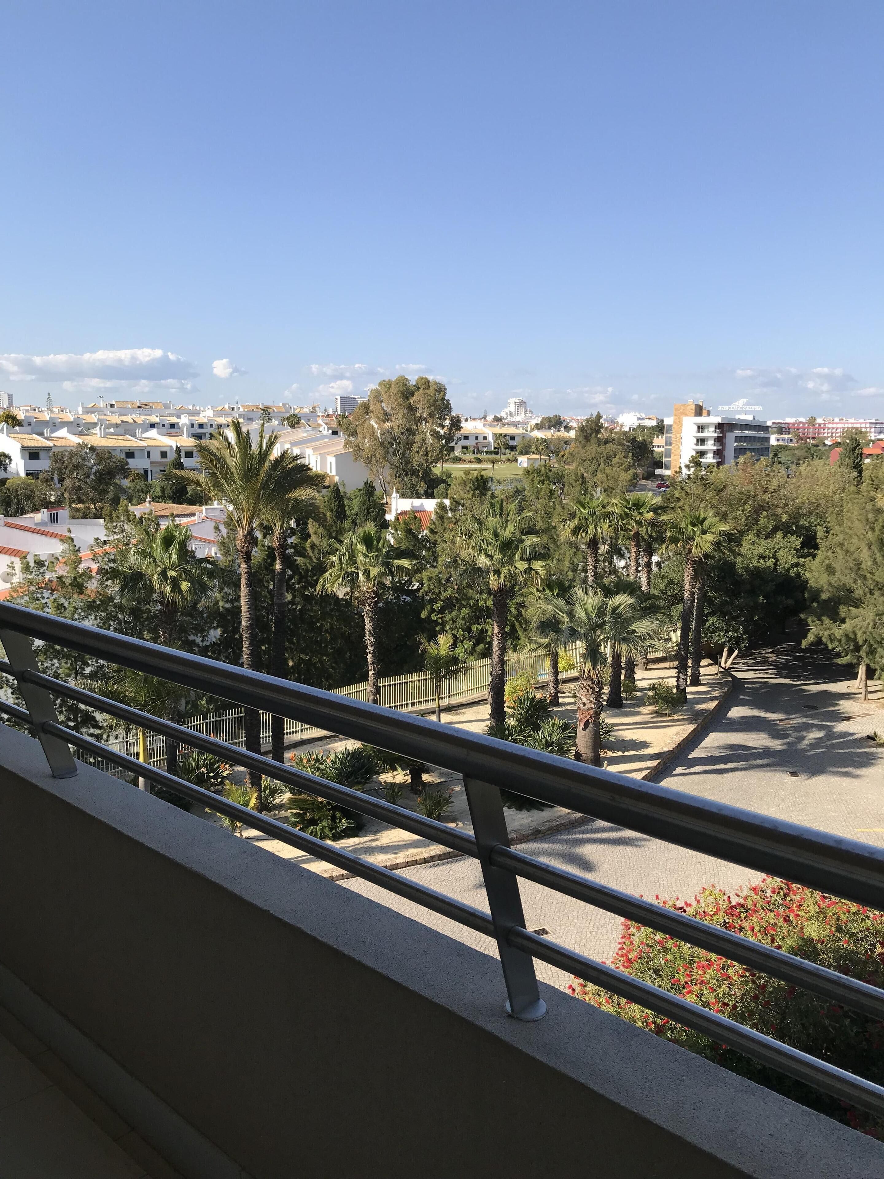 Ein Balkon mit Metallgeländer, der auf ein Wohngebiet mit Häusern, Bäumen und blauem Himmel blickt.