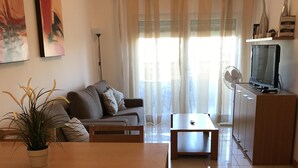 A living room with a sofa, a dining table, a TV, and a plant. - Outstading Executive Apartment 150 metres from the beach (Albufeira)