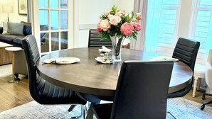 A modern dining area with a round table, black chairs, a vase with flowers, and a contemporary light fixture. - Comfy & Quiet Bungalow -Pet Friendly! 30+ Nt min.  Summer 2026 Special! (Houston)