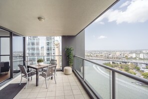 A balcony with a dining table, chairs, a potted plant, and a view of a river and cityscape.
