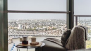 A view from a window overlooking a cityscape with a bridge, a table with a cup, and a sofa. - Sky Homes on Queen (Brisbane)